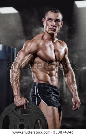 Professional bodybuilder with weight disk in gym. Weightlifter with naked torso and the disk in the hands. Fitness male model