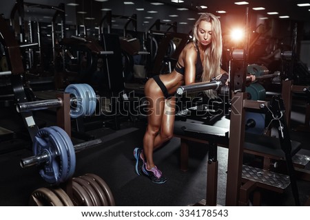 Blonde fitness bikini girl with perfect shape body rests after sport workout in gym and leaning on bar
