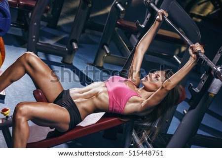 Sexy athletic sport girl with perfect fitness body doing workout hard training with bar on incline bench in the gym
