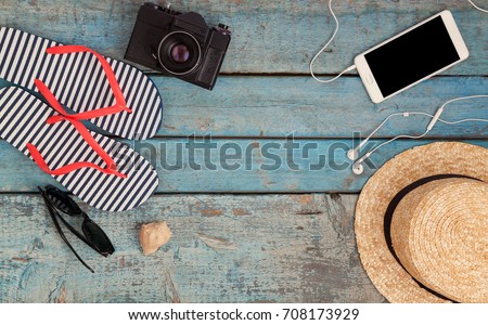 Still life of different items for relaxing on the beach, rubber flip-flops, hat, camera, phone, sunglasses, headset on a wooden blue background. Concept of a youth trip, rest on the beach