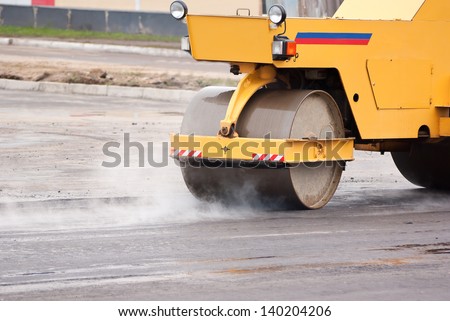 Small yellow road roller smoothes hot asphalt