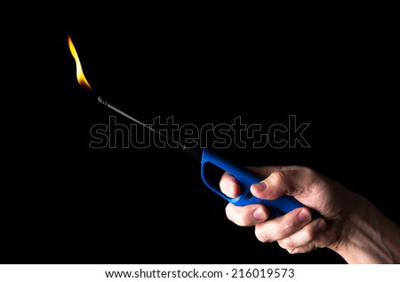 Burning gas lighter in a man\'s hand isolated on black background