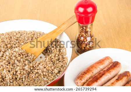 Boiled buckwheat in pan with ceramic coating, grilled sausage and spice on table