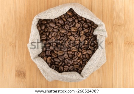 Burlap bag of coffee beans roasted coffee on wooden table, top view