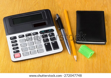 Electronic calculator, notepad, pen, sharpener  and pencil on wooden table