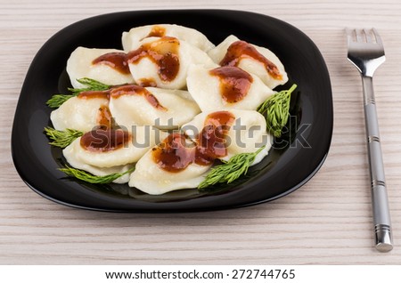 Boiled dumplings in black glass plate and metallic fork on table
