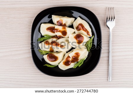 Boiled dumplings in black glass plate and metallic fork on table, top view
