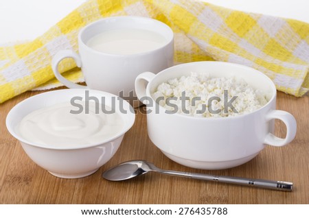 Sour cream, milk and cottage cheese and napkin on bamboo board