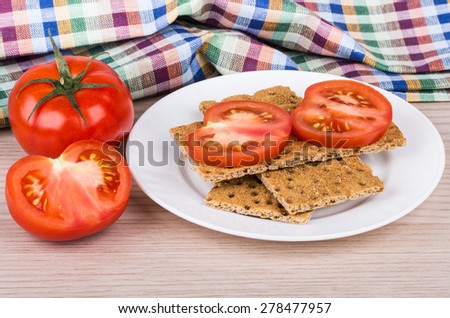 Wheat crisp bread in plate, tomatoes and towel on wooden table