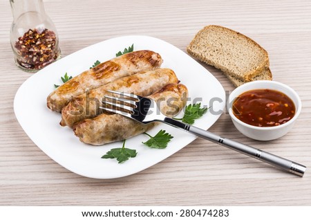 Fried pork sausages with parsley in glass plate, pepper, fork, bread and ketchup on wooden table