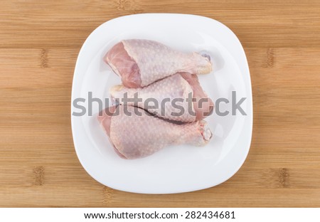 Three raw chicken legs in white glass plate on wooden bamboo board