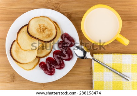Pancakes and raspberry jam in plate, cup of milk on table, top view