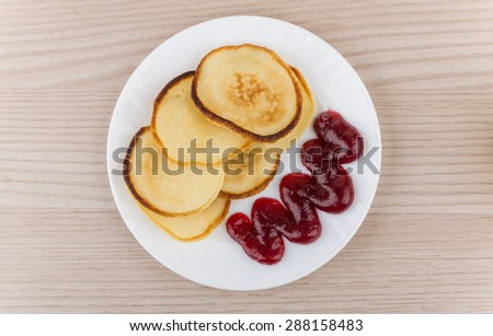 Pancakes with raspberry jam in glass plate on wooden table, top view
