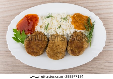 Fried cutlet with rice, squash caviar, ketchup and greens in dish on table. Top view