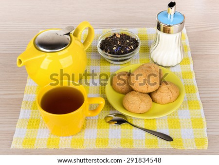 Kettle and cup of hot tea, sugar and biscuits on checkered napkin
