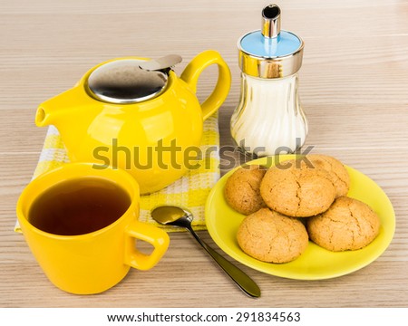 Yellow tea cup with tea and cookies on wooden table