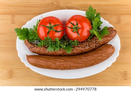 Smoked sausage, tomatoes and parley in glass dish on bamboo board, top view