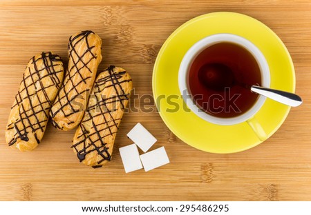 Eclairs, black tea in cup and lumpy sugar on wooden table, top view