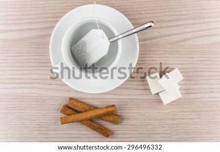 Cup with tea bag, cinnamon sticks and pieces of sugar on wooden table, top view