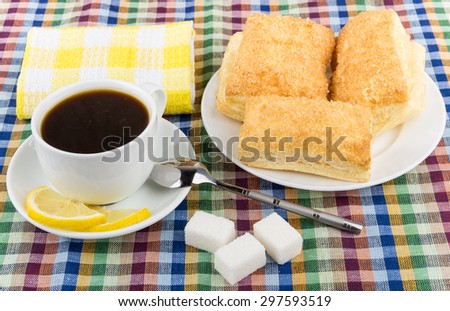 Coffee, lemon and sugar, plate with flaky biscuits on checkered tablecloth