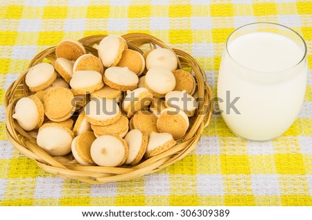 Heap of cookies with egg glaze in wicker basket and glass milk on yellow tablecloth