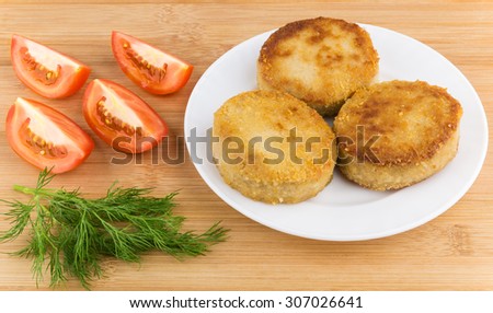 Sliced tomatoes, dill and fried meatballs in plate on bamboo table
