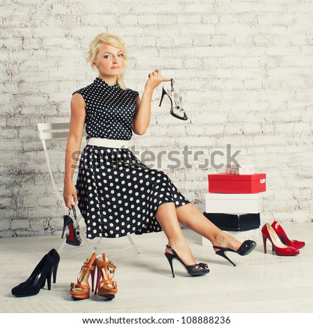 Young blonde woman in fashioned dress sitting in a chair in the store and choosing shoes (make shopping)