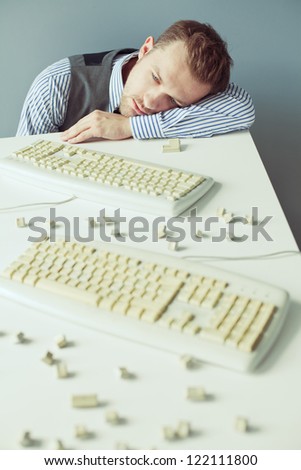 Young computer geek with beard in suit lying on the table with disassembled keyboards