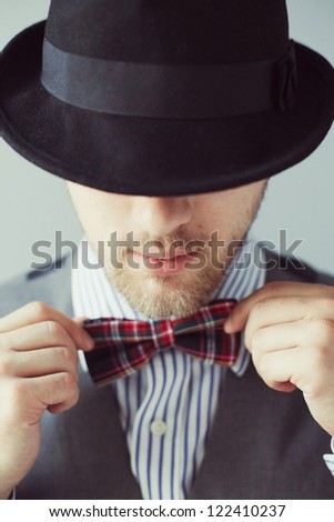 Portrait of a man in the black hat correcting bowtie