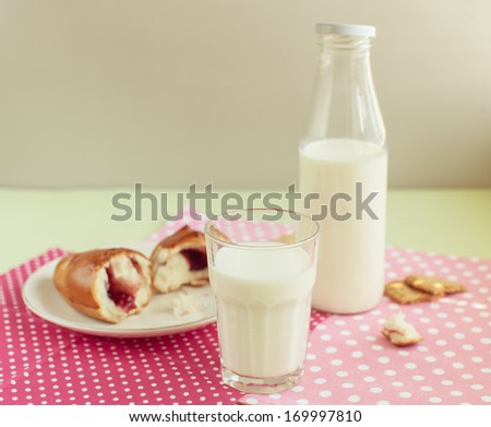 Tasty breakfast - milk, cookies and roll with jam in front of pink and green background