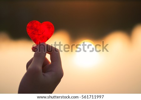 hand is raising the red paper heart with blur sunlight reflect on river ,Valentines day