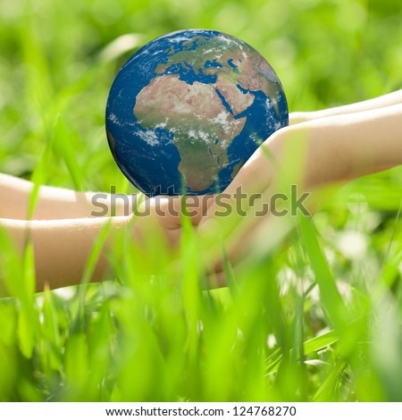 Earth in children`s hands against green grass blurred background. Elements of this image furnished by NASA