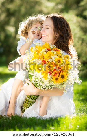 Happy child and woman with bouquet of spring flowers sitting on green grass. Mother`s day concept