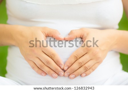 Pregnant woman holding hands on belly in shape of heart
