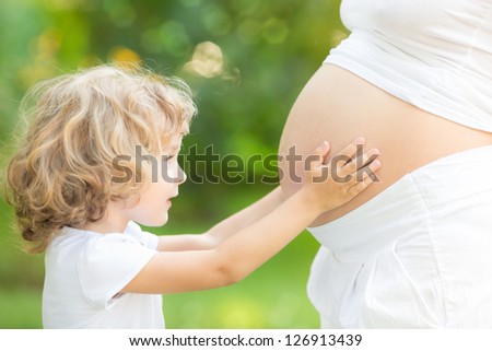 Happy child holding belly of pregnant woman against green spring background