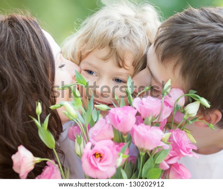 Happy family with bouquet of spring flowers. Mother and father kissing your child against natural green background. Celebration concept
