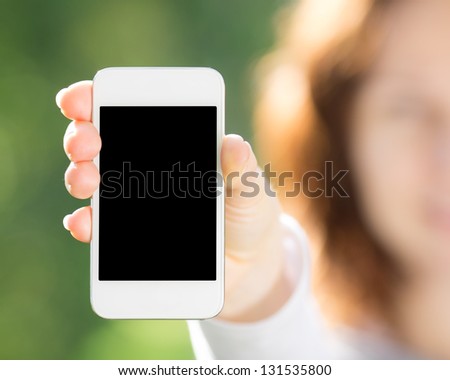Woman Holding Smart Phone In Hand Against Green Spring Background. Blank Screen With Copyspace