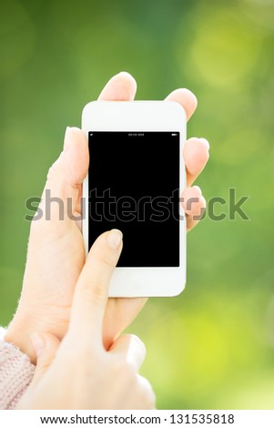 Woman holding smart phone in hands against green spring background. Blank screen with copy space for your text
