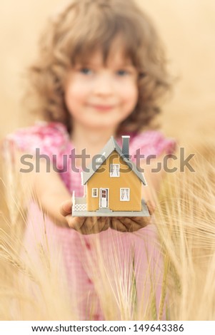 Happy child holding house in hands against autumn yellow background. Real estate concept
