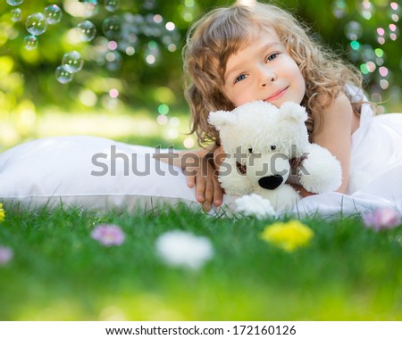 Happy child with toy teddy bear on green grass outdoors in spring garden