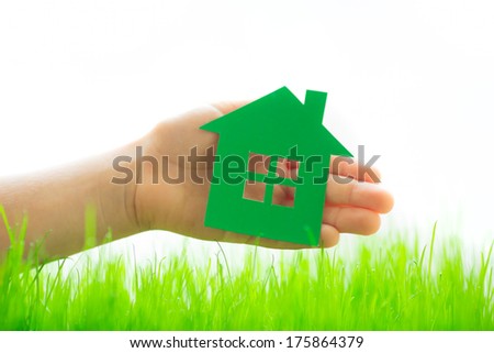Green paper house in hand over spring grass