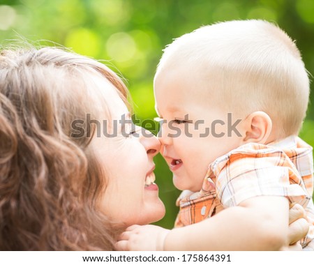 Happy mother and baby boy having fun outdoors in spring park against natural green background