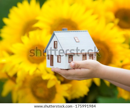 House in children`s hands against autumn yellow background. Real estate concept