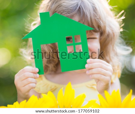 Paper house in hand against spring green background. Real estate concept