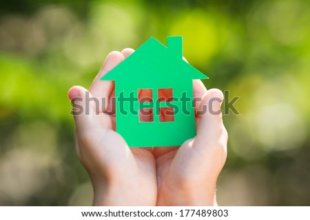 Child holding paper house in hands against spring green background