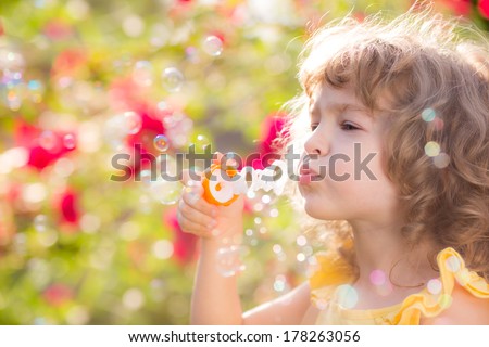 Happy child blowing soap bubbles outdoors in spring park