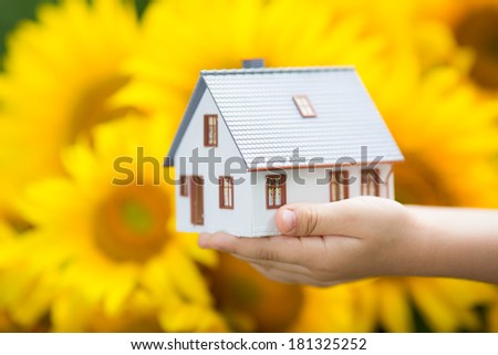 House in hand against spring flower background. Real estate concept