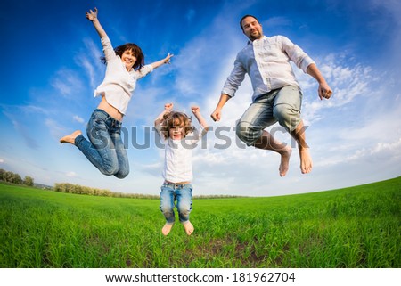 Happy family jumping in green field against blue sky. Summer vacation concept