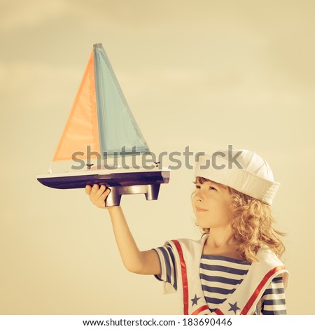 Happy kid playing with toy sailing boat against summer sky background. Travel and vacations concept