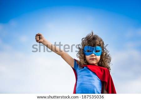 Superhero child against blue summer sky background. Kid having fun outdoors. Girl power and feminism concept